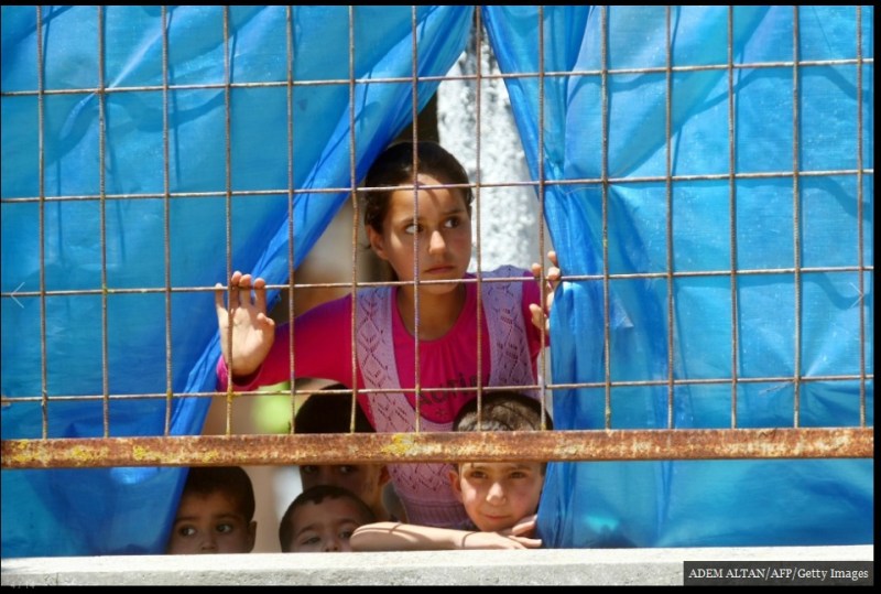 ينظر الأطفال اللاجئون السوريون من خلال الجدار إلى المخيم في بلدة Yayladagi على الحدود التركية في محافظة Hatay في 26 يونيو/ حزيران 2011. بالرغم من حقيقة أن نحو 12,000 لاجئ سوري احتموا في تركيا في ذلك الوقت، إلا أنه لم يمتثل سوى بضع مئات إلى دعوات الأسد للعودة إلي منازلهم في ذلك الصيف.