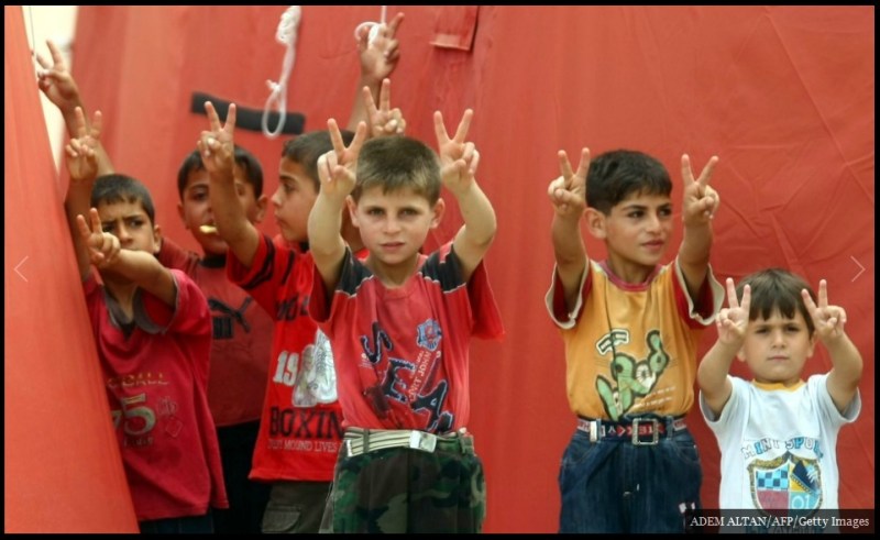 لاجئون سوريون أطفال يرسمون رموز السلام من وراء سياج المخيم بالقرب من الحدود التركية Yayladagi.