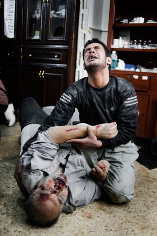 رجل سوري يمسك يد أخيه الجريح في منزل مستعمل كمشفى في بابا عمرو، أحد الأحياء الواقعة في جنوب حمص. 6 فبراير/ شباط 2012