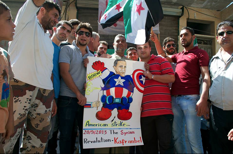 صور الرئيس أوباما بطلاً خارقاً نفست عضلاته المنتفخة بسهولة عن طريق دبوس، في مظاهرة في كفرنبل. ينتقد العديد من النشطاء السوريين الولايات المتحدة بسبب ما يصفونه بالدعم الباهتة للجماعات المتمردة في البلاد.
